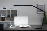 Black LED desk lamp with adjustable arm on dark desk with open book, modern office lighting