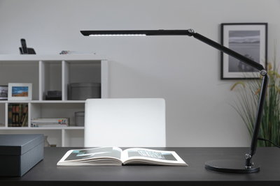 Black LED desk lamp with adjustable arm on dark desk with open book, modern office lighting