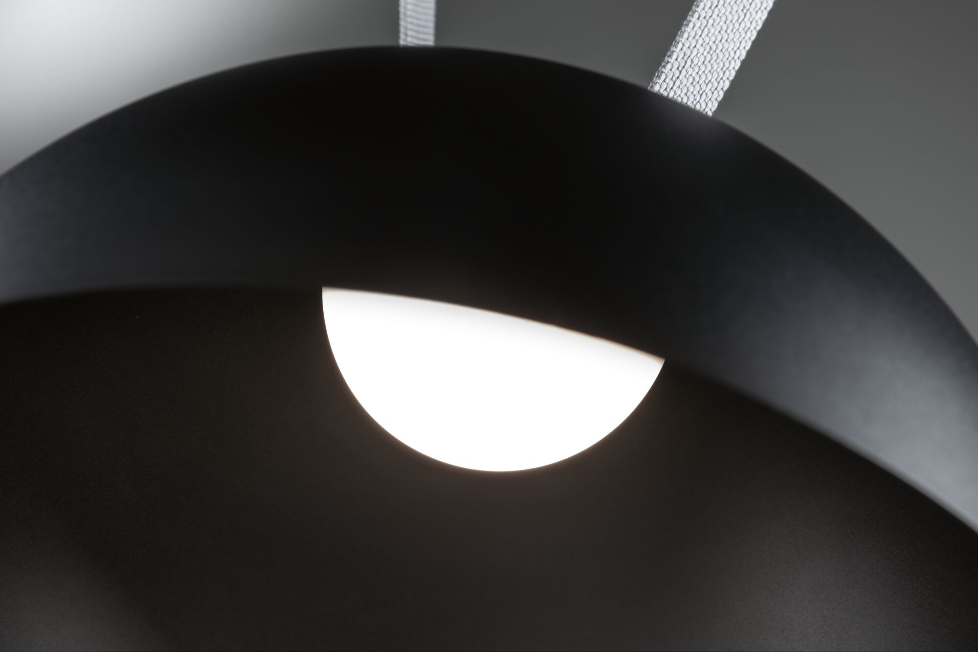 Black metal pendant lamp with white LED light and textile suspension for modern lighting design.