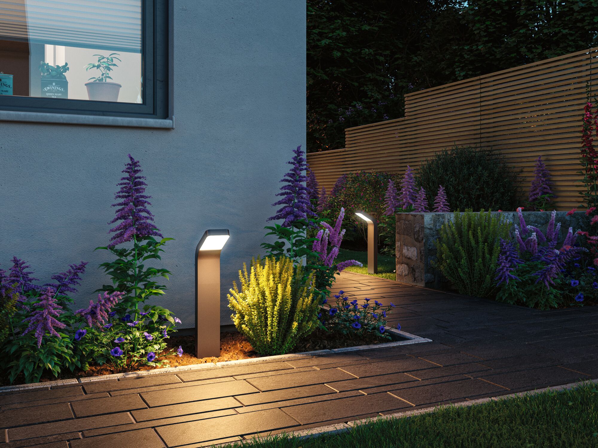 Moderne anthrazitfarbene LED-Wegeleuchte aus Metall beleuchtet Gartenweg mit bunten Blumen bei Dämmerung