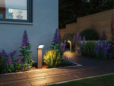 Moderne anthrazitfarbene LED-Wegeleuchte aus Metall beleuchtet Gartenweg mit bunten Blumen bei Dämmerung
