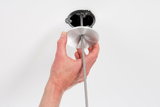 Hand holding round aluminum ceiling mount with grey fabric cable for lamp installation on white ceiling