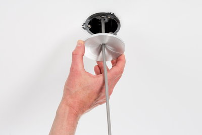 Hand holding round aluminum ceiling mount with grey fabric cable for lamp installation on white ceiling