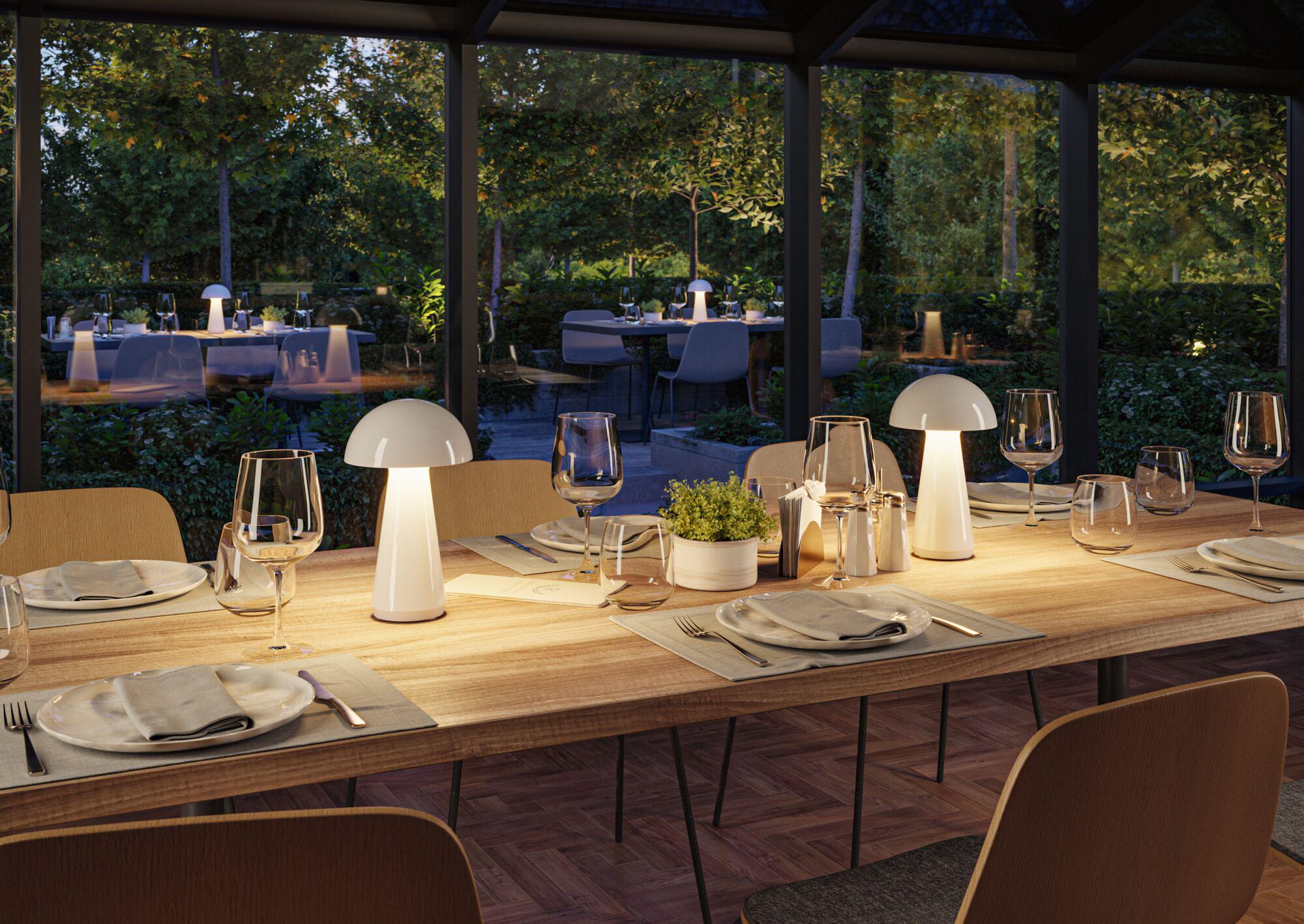 Modern dining room with two white LED table lamps on light wooden table set with dishes