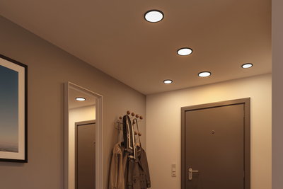 Plafonniers LED ronds et plats en lumière blanche chaude éclairent un couloir moderne avec porte-manteau et miroir.