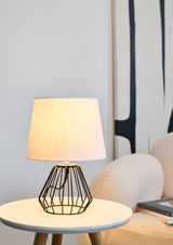 Moderne Tischlampe mit schwarzem Metallgestell und weißem Stoffschirm auf rundem Beistelltisch