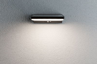 Zwarte metalen LED-wandlamp met bewegingssensor op grijze muur voor buitenverlichting