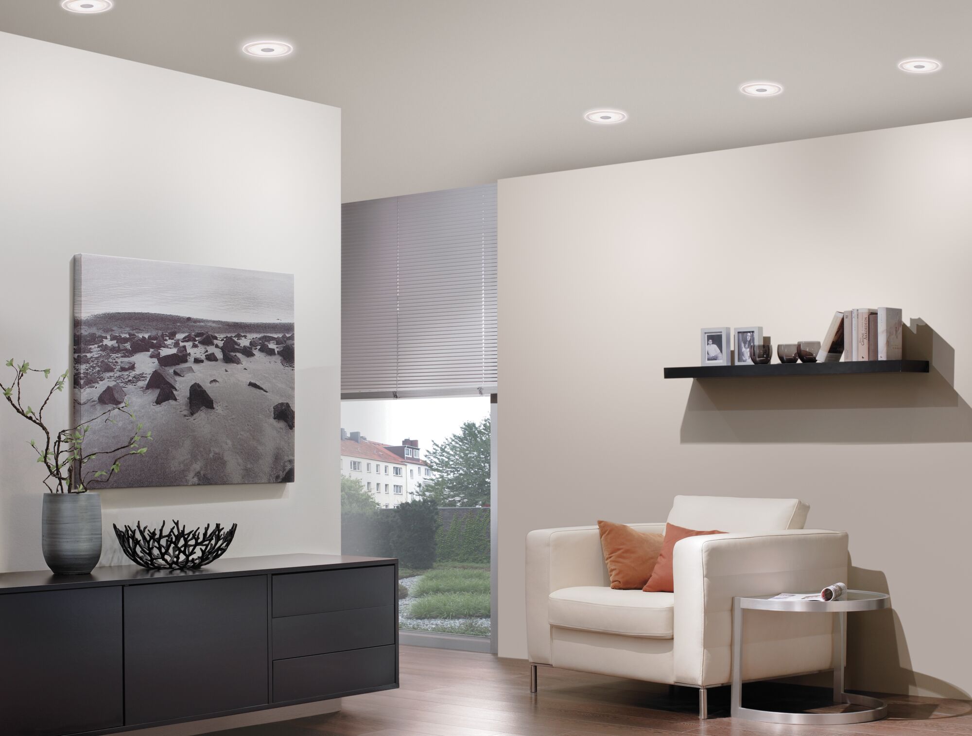 Moderne woonkamer met witte leren fauteuil, zwarte dressoir en ronde witte plafondlampen.