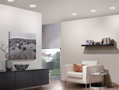 Moderne woonkamer met witte leren fauteuil, zwarte dressoir en ronde witte plafondlampen.