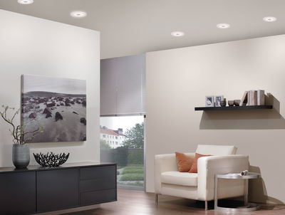 Moderne woonkamer met witte leren fauteuil, zwarte dressoir en ronde witte plafondlampen.