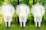 Three clear glass LED bulbs emitting warm white light with a green forest background
