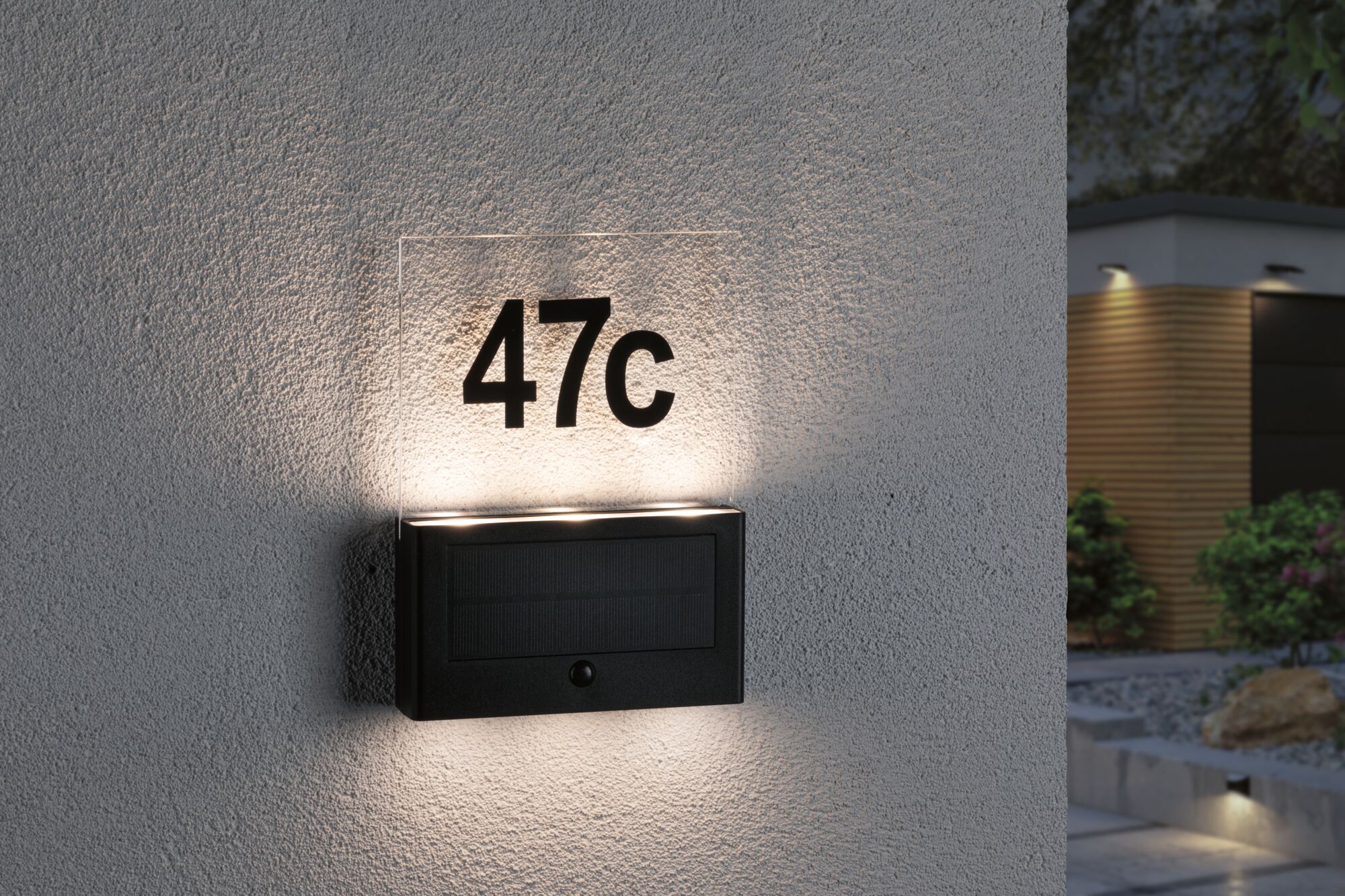 Schwarze Solar-Hausnummernleuchte mit beleuchteter Glasplatte und Ziffer 47c an grauer Wand außen