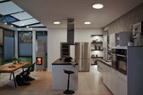 Modern kitchen with white gloss cabinets, black countertop and round ceiling lights emitting warm white light