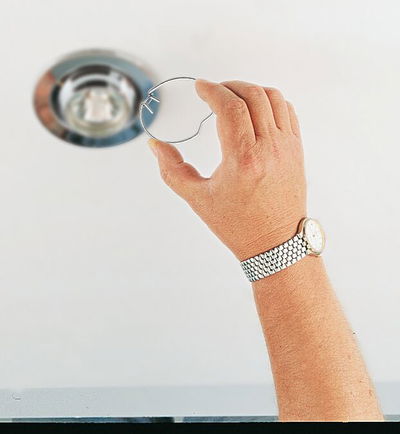 Hand holding silver metal spring clip near built-in ceiling LED spotlight fixture.