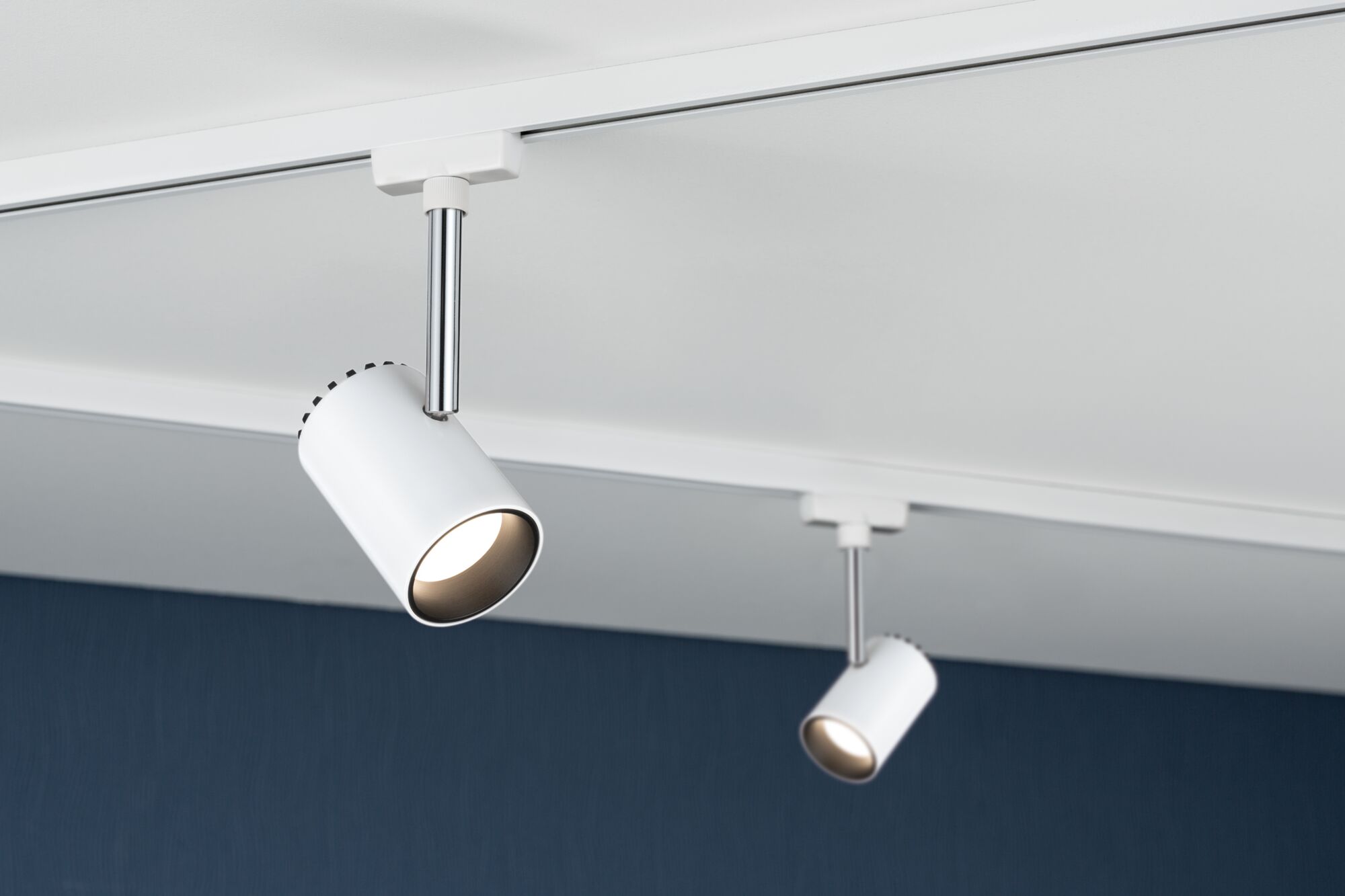 Two white metal LED spotlights on track system mounted on white ceiling for modern lighting