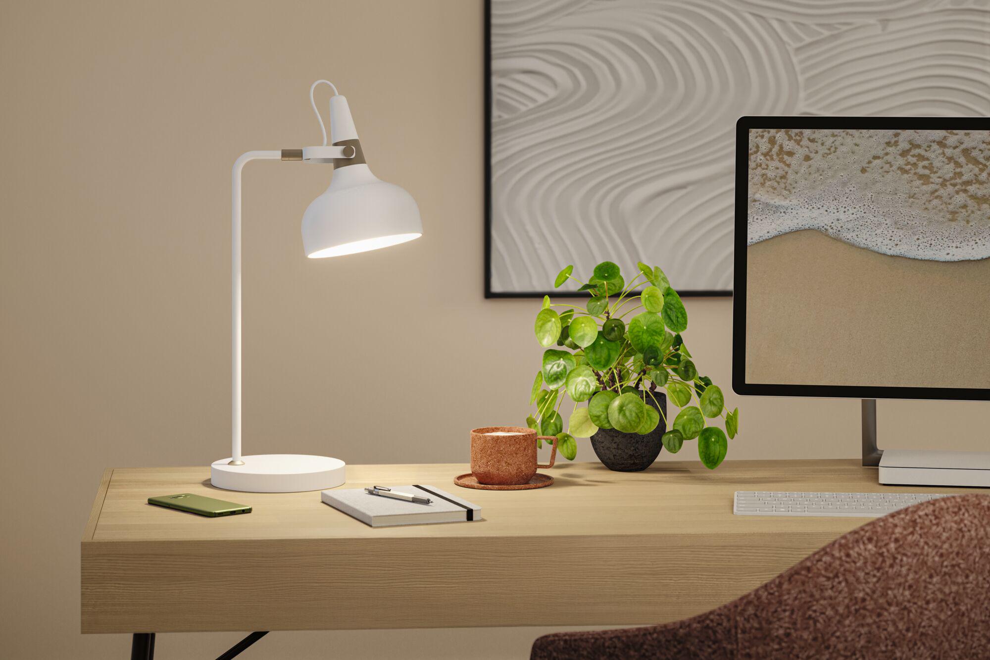 White metal desk lamp with adjustable head on light wood desk in office workspace