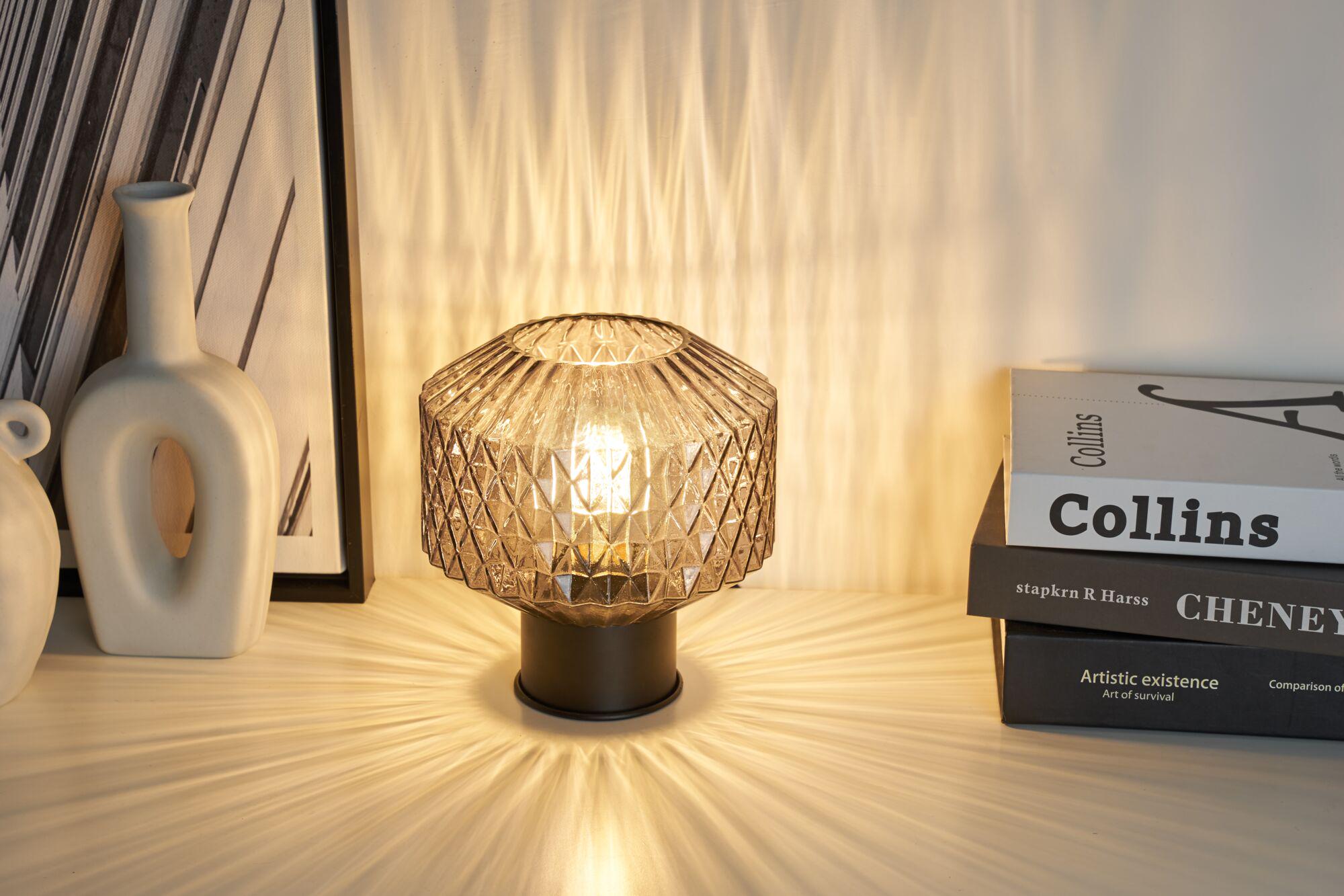 Table lamp with smoked glass and black metal base casting decorative light patterns on surfaces.
