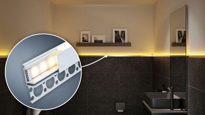 Hvid LED-vægprofil med varmt hvidt lys i moderne badeværelse med mørke fliser og spejl.