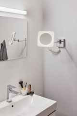 Modern LED wall mirror with chrome arm and square light ring in bathroom setting.