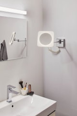 Moderne LED-wandspiegel met chromen arm en vierkante verlichtingsring in badkamer.