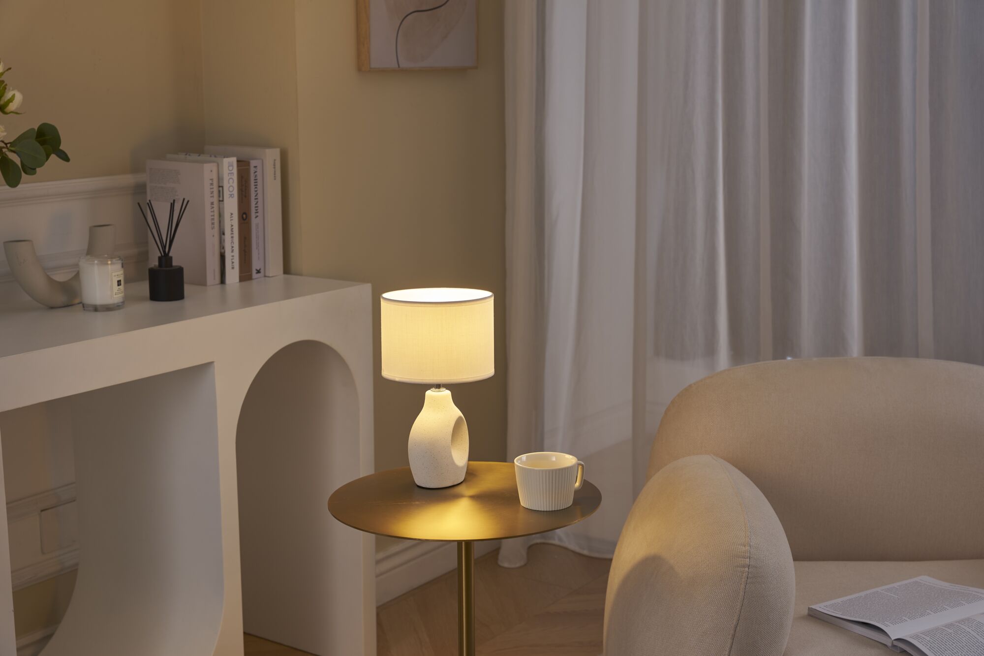 Lit table with cream ceramic lamp and cup beside beige sofa in cozy living room setting