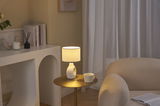 Lit table with cream ceramic lamp and cup beside beige sofa in cozy living room setting