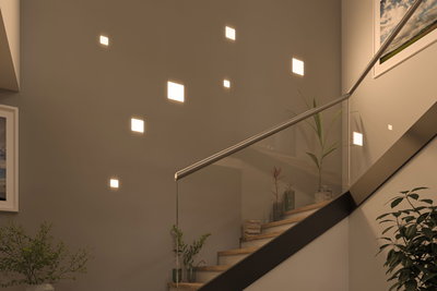 Moderne quadratische LED-Wandlichter in warmweiß an Treppenhauswand mit Glasgeländer und Pflanzen.