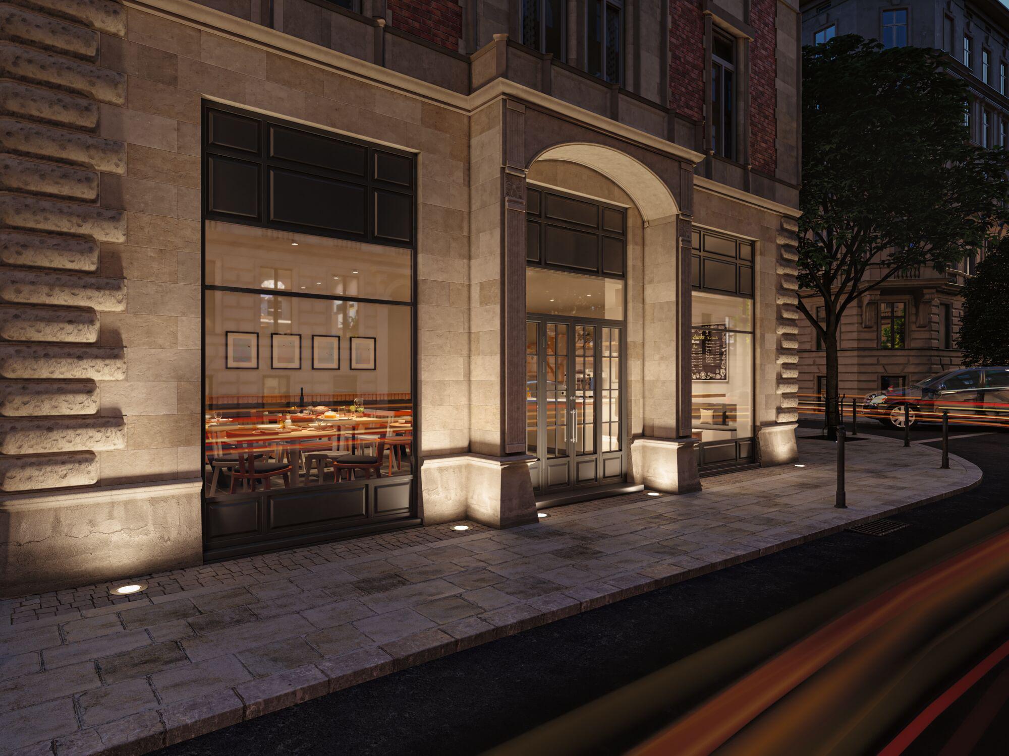 Lit entrance of building with grey stone facade and large windows, atmospheric outdoor lighting at dusk