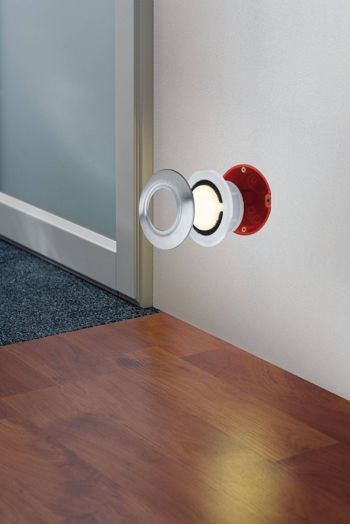 Recessed LED floor spotlight with stainless steel ring and red housing mounted on wall near wooden floor