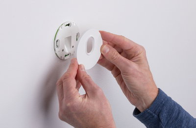 Hands installing white plastic wall mount with oval cutout on smooth wall for LED lighting fixture
