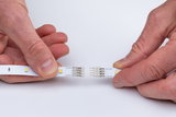 Handen verbinden twee witte LED-strips met 12V DC-connectoren voor flexibele verlichting