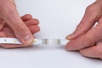 Hände verbinden zwei weiße LED-Streifen mit 12V DC-Anschluss für flexible Lichtinstallation