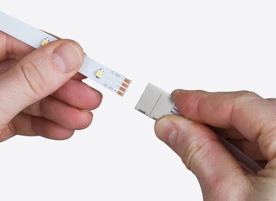 Hand verbindet weißen LED-Streifen mit Kunststoff-Steckverbinder für LED-Beleuchtungssysteme