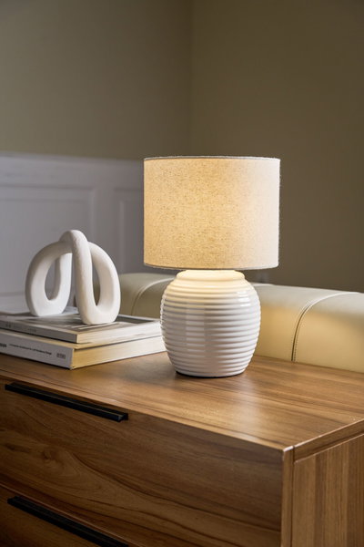 White ceramic table lamp with beige fabric shade on wooden dresser, modern home decor