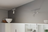 Spot câble métallique blanc moderne sur mur gris au-dessus d'un meuble de cuisine blanc avec vaisselle.