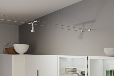 Moderner weißer Seilstrahler aus Metall an grauer Wand über weißem Küchenschrank mit Geschirr.