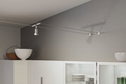 Moderner weißer Seilstrahler aus Metall an grauer Wand über weißem Küchenschrank mit Geschirr.