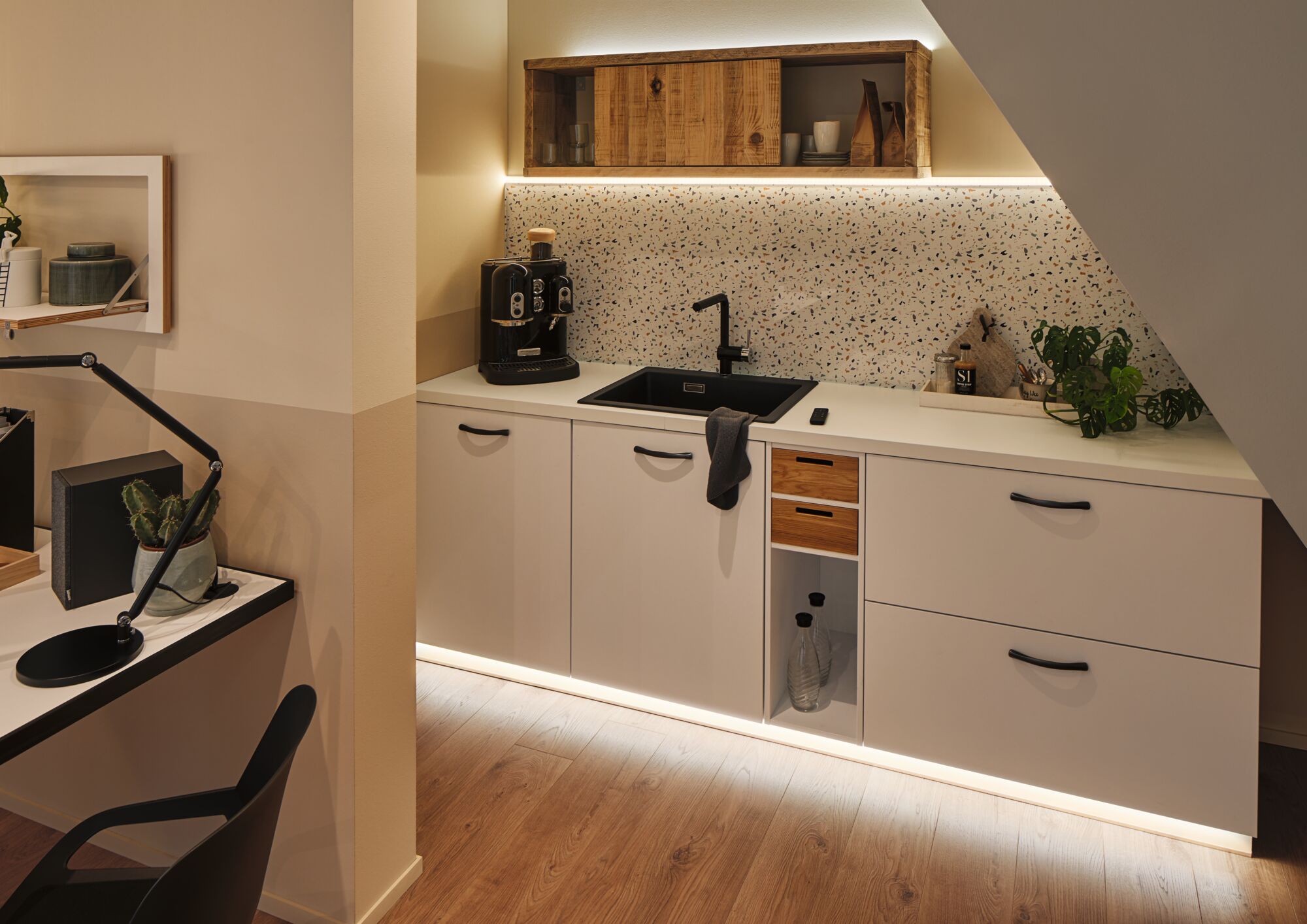 Cuisine moderne blanche avec évier noir, étagère en bois et éclairage LED sous le plan de travail.