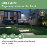 Moderne schwarze LED-Gartenleuchten mit warmweißem Licht auf Rasenweg vor Terrasse mit Sitzmöbeln