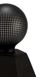 Black metal sphere with perforated pattern on square base, modern decorative object
