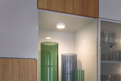 Rundes weißes LED-Deckenlicht in Küchenregal mit grünen und grauen Glasvasen und Gläsern.