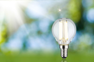 LED-Glühbirne mit klarem Glas und silbernem Sockel vor unscharfem grün-blauem Hintergrund