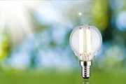 LED-Glühbirne mit klarem Glas und silbernem Sockel vor unscharfem grün-blauem Hintergrund