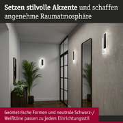 Moderne schwarze LED-Wandleuchten mit geometrischem Design an grauer Wand im Flur mit Spiegel und Pflanzen