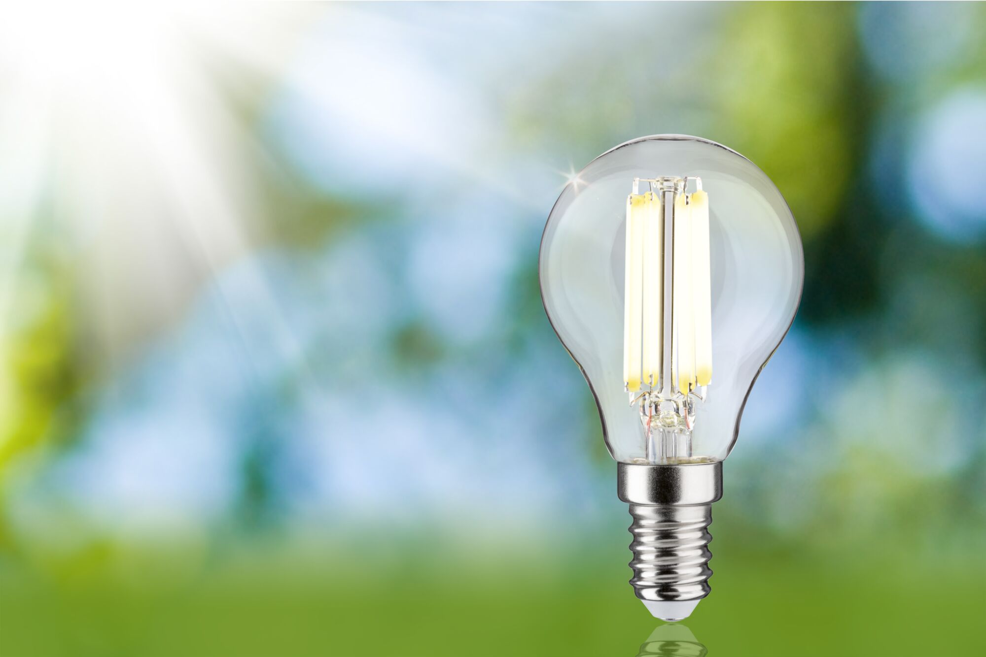 Klassieke LED-lamp met helder glas en zilveren voet tegen een groen-blauwe wazige achtergrond