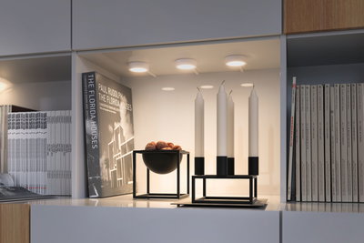 Moderne weiße Regalbeleuchtung mit drei runden LED-Deckenleuchten und schwarzem Kerzenhalter mit weißen Kerzen