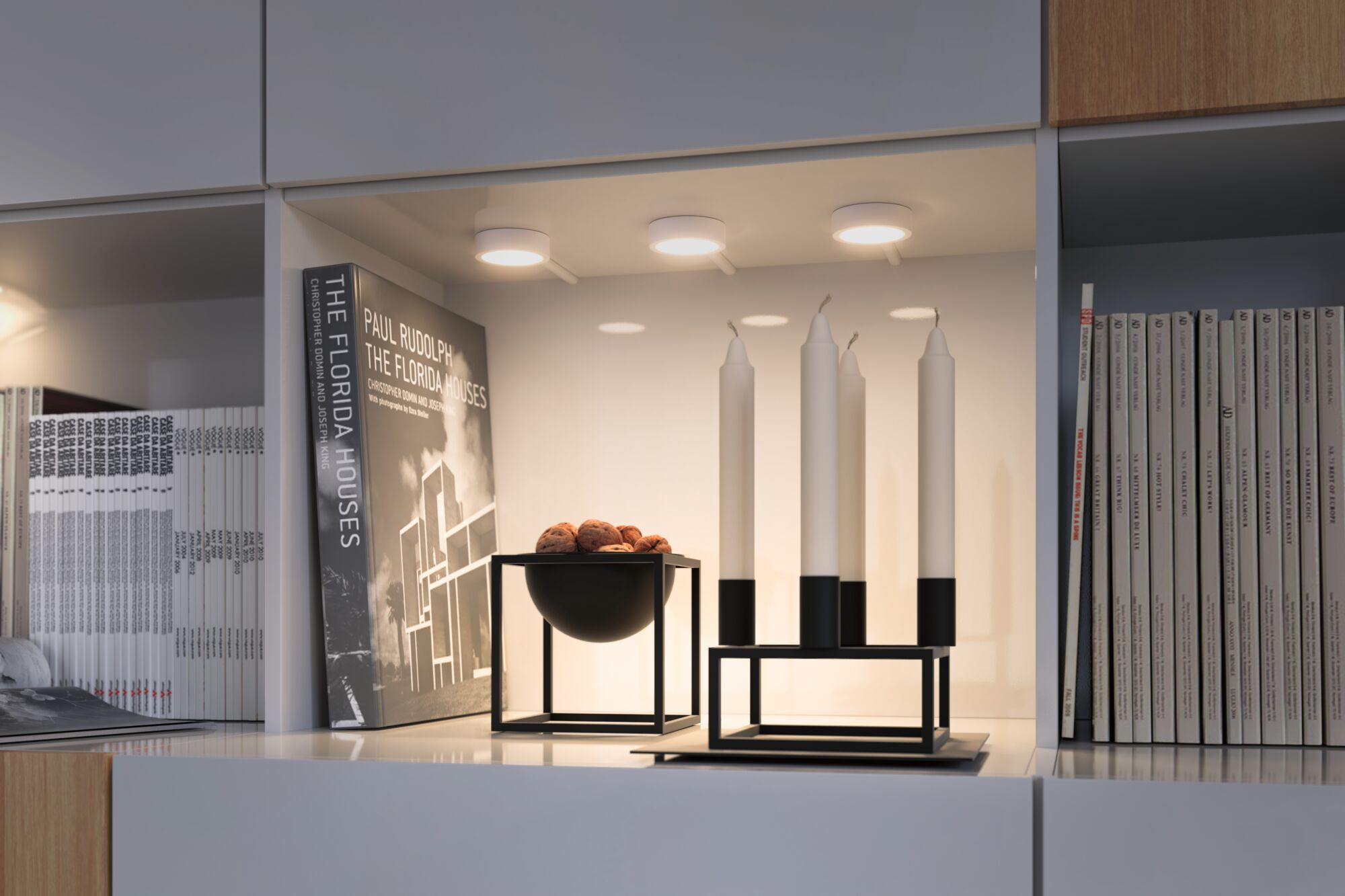 Moderne weiße Regalbeleuchtung mit drei runden LED-Deckenleuchten und schwarzem Kerzenhalter mit weißen Kerzen