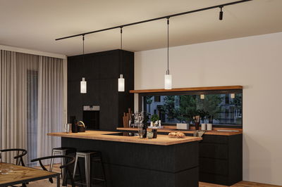 Moderne Küche mit schwarzer Holzfront und Holzarbeitsplatte, drei weißen Pendelleuchten an schwarzer Schiene.