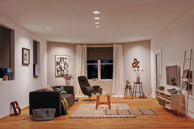 Salon moderne avec sol en bois, fauteuil noir, canapé et éclairage LED blanc chaud au plafond.