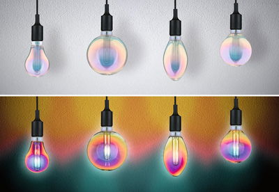 Vier bunte LED-Glühbirnen mit schwarzem Sockel an weißer und bunter Wand für dekorative Beleuchtung
